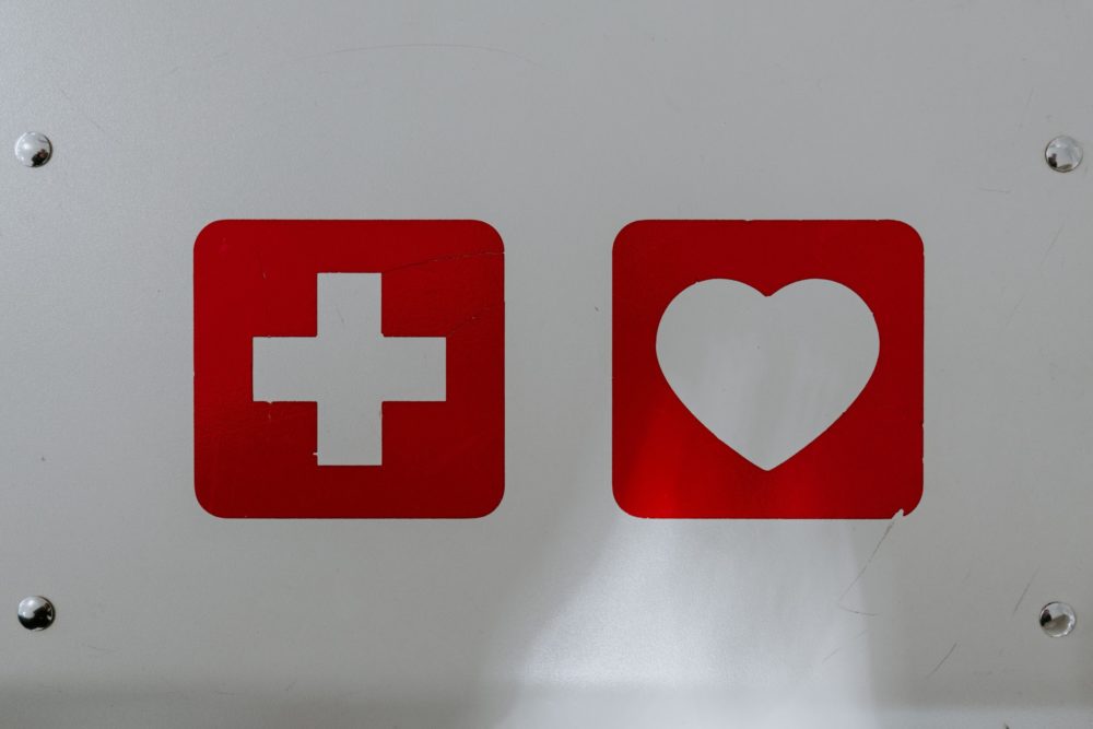 Image of a white plus sign on a red background and a white heart on a red background on a metal sign