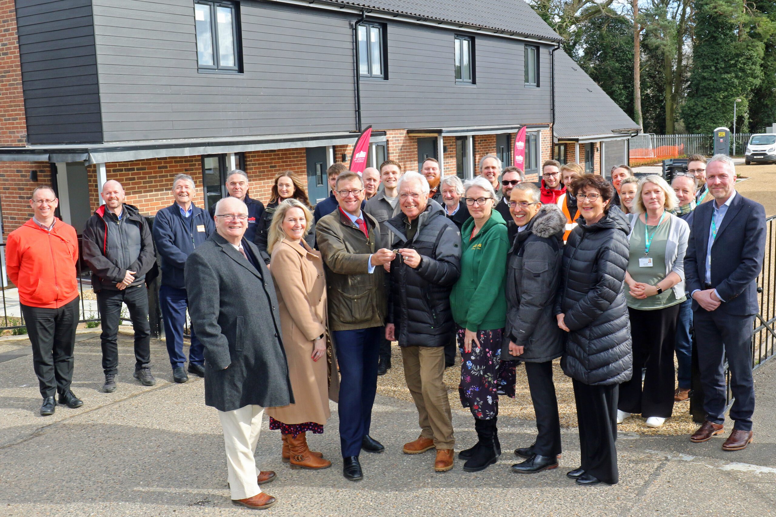 Members of Breckland District Council and Broadland Housing accepting keys to the new homes with people in backbround